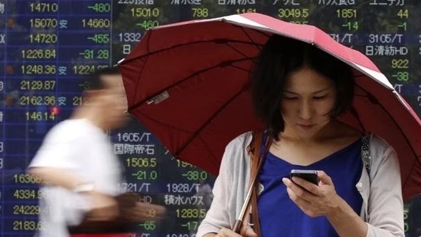 A woman holding an umbrella looks at her cellphone in front of an electronic board showing the various stock prices outside a brokerage in Tokyo A woman holding an umbrella looks at her cellphone in front of an electronic board showing the various stock prices outside a brokerage in Tokyo