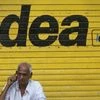 A man speaks on his mobile phone as he sits in front of a shop displaying the Idea Cellular Ltd's logo on its shutter in Mumbai
