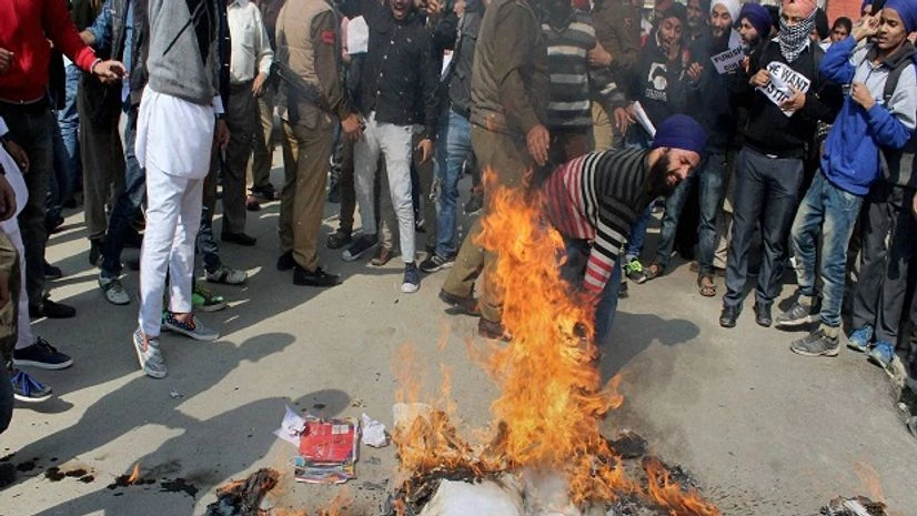 Sikh protesters trampling the burning effigy of Parkash Singh Badal-led government, as a police officer tries to stop them during their protest against the alleged desecration of religious book and Punjab firing incident, at Lal Chowk in Srinagar. Sikh protesters trampling the burning effigy of Parkash Singh Badal-led government, as a police officer tries to stop them during their protest against the alleged desecration of religious book and Punjab firing incident, at Lal Chowk in Srinagar.