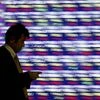 A man, holding a mobile phone, walks past an electronic stock quotation board outside a brokerage in Tokyo, Japan