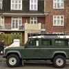 A man walks past a Land Rover Defender parked on a street in London