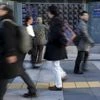 A man looks at an electronic stock quotation board as passers-by walk past, outside a brokerage in Tokyo