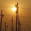 A worker is silhouetted against the setting sun while installing an overhead electric cable pole on the banks of river Ganges, Allahabad