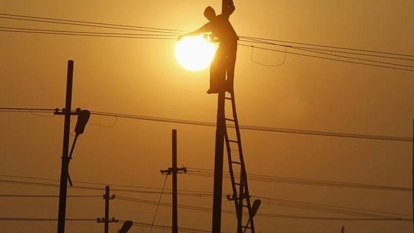 A worker is silhouetted against the setting sun while installing an overhead electric cable pole on the banks of river Ganges, Allahabad A worker is silhouetted against the setting sun while installing an overhead electric cable pole on the banks of river Ganges, Allahabad