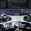 Traders work at their desks in front of the German share price index