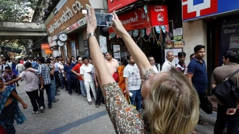 A foreign tourist takes pictures of people standing in a queue outside a bank to exchange and deposit their old, high denomination banknotes in Kolkata A foreign tourist takes pictures of people standing in a queue outside a bank to exchange and deposit their old, high denomination banknotes in Kolkata