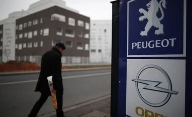 opel, peugeot A man walks past the logos of French car maker Peugeot and German car maker Opel