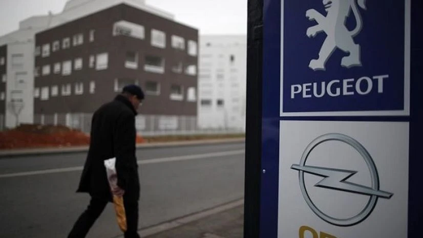 opel, peugeot A man walks past the logos of French car maker Peugeot and German car maker Opel