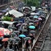 Stream of people open their umbrellas to save themselves from rain, as they walk beside the railway tracks at Ballygunge Junction station, in Kolkata