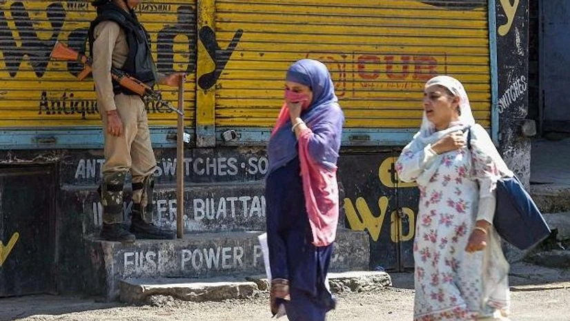 kashmir Women walk past a CRPF person standing guard in a street in Srinagar, Thursday