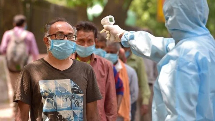lockdown, coronavirus A man wearing protective suit checks the temperature of people standing in a queue to get free food at IYC headquarters, during the nationwide COVID-19 lockdown, in New Delhi