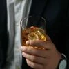 Man holding glass of whiskey with ice cubes on black background, closeup