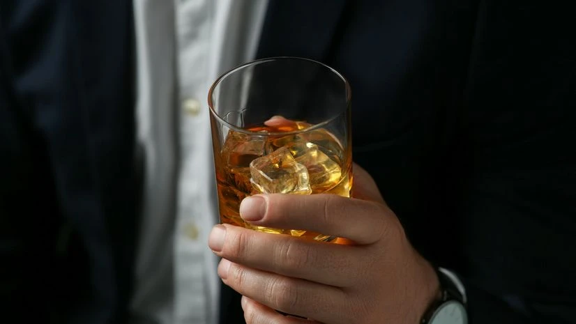 alcohol, liquor Man holding glass of whiskey with ice cubes on black background, closeup