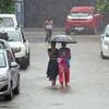 Women use an umbrella and not wearing a mask during a rain shower, in New Delhi on Wednesday. (