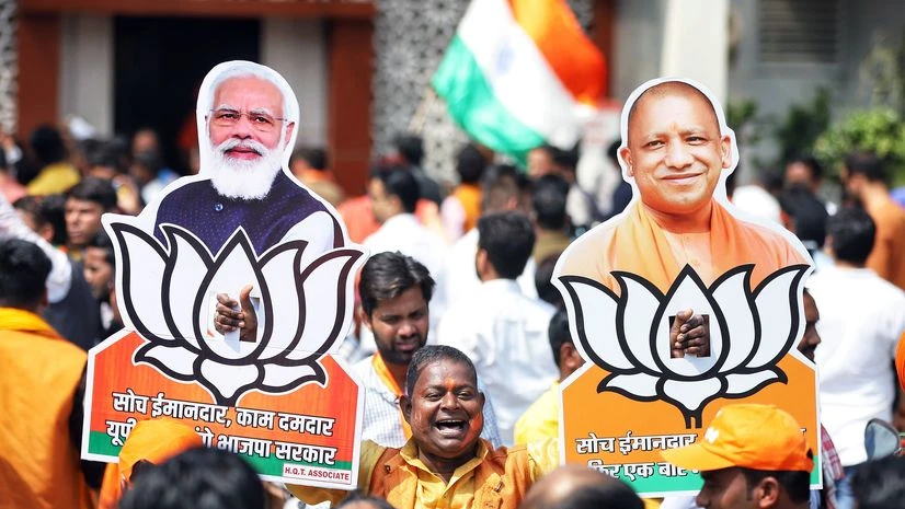 UP elections, Yogi Adityanath A BJP supporter holds the cutouts of Prime Minister Narendra Modi and Uttar Pradesh Chief Minister Yogi Adityanath during the celebration as the party leads in State Assembly elections, at the state party office, in Lucknow.